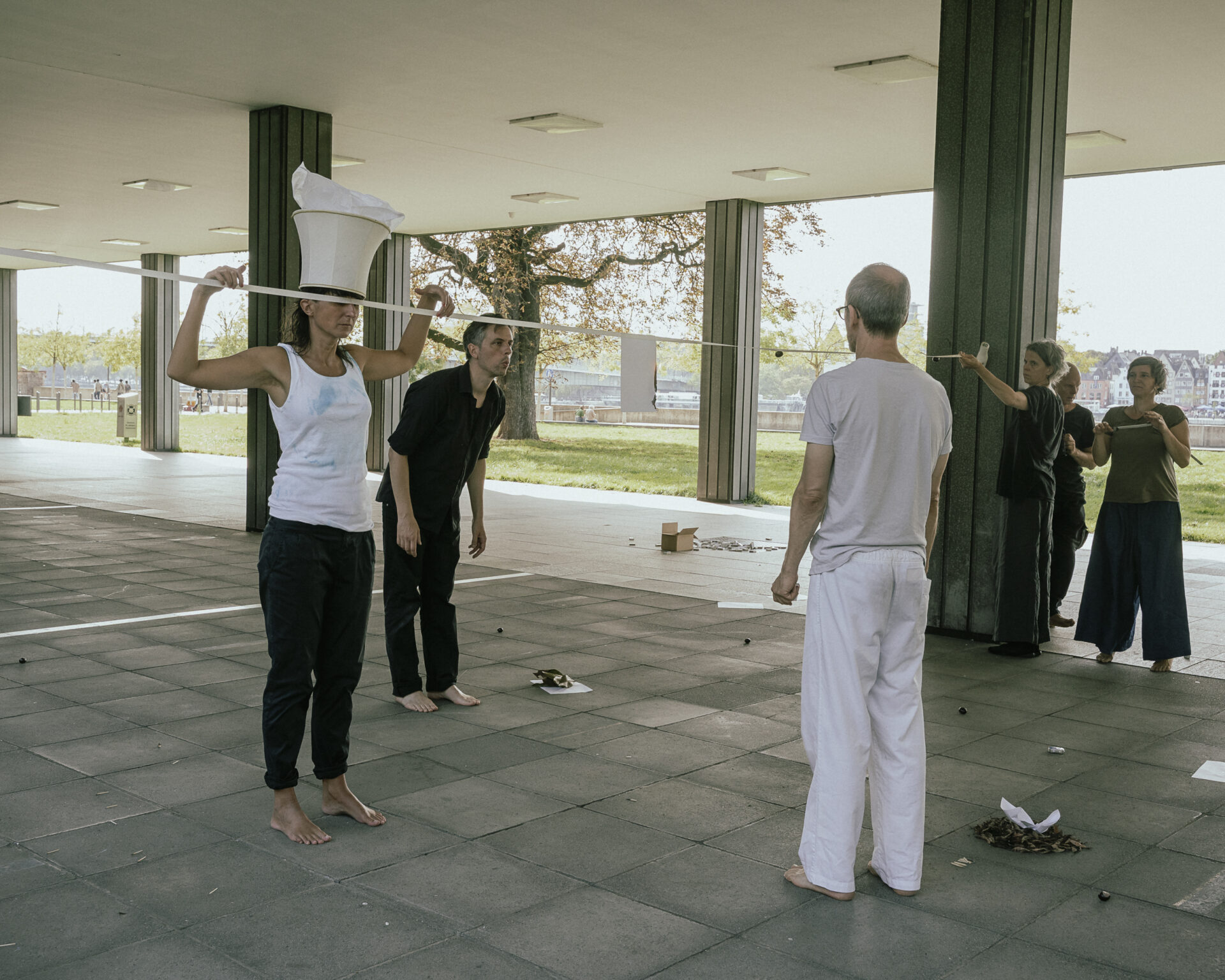 Five performers engage in a playful, collaborative activity in a spacious, sunlit area, creating a dynamic atmosphere with movement.