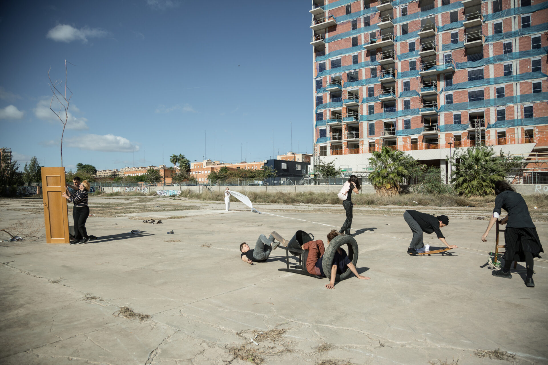 People interacting in an abandoned urban space, with some kneeling or sitting on the ground, and a speaker at a podium nearby.