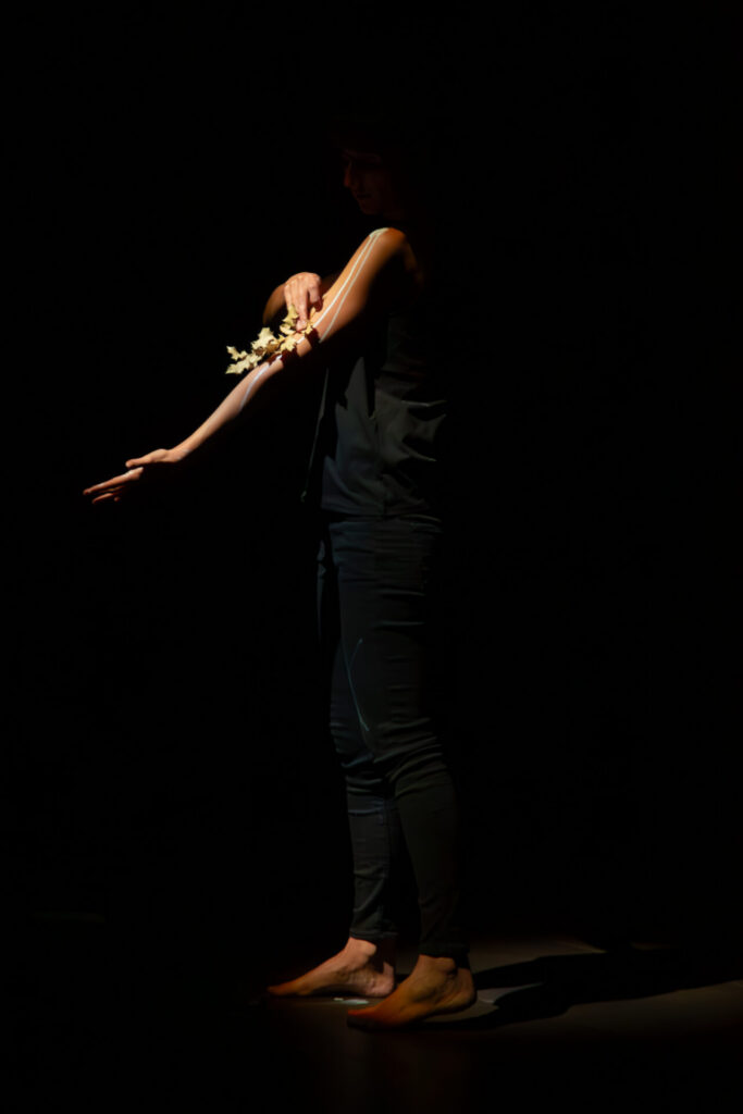 A silhouetted figure in dark clothing extends an arm adorned with a floral accessory, evoking a sense of quiet elegance.